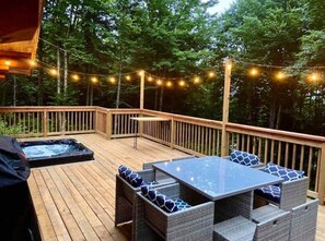 A wooden deck with a hot tub, outdoor furniture, and string lights. - Le Rondin, Log cabin with spa, 5 min from Valcartier Vacation Village (Saint-Gabriel-de-Valcartier)