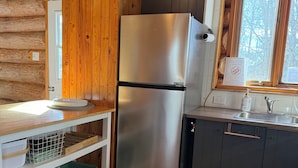 Ett kök med ett kylskåp i rostfritt stål, träskåp, ett fönster med utsikt och ett klinkergolv.
