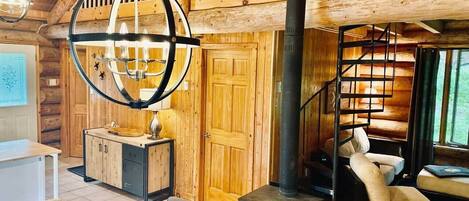 A wooden cabin interior with a dining area, a staircase, and a large window.