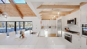 Eine moderne Küche mit weißen Schränken, einem Edelstahl-Kühlschrank und einem großen Fenster mit Blick auf eine verschneite Landschaft.
