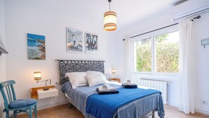 Une chambre à coucher comprenant un lit, des tables de chevet, une chaise, une fenêtre avec des rideaux et des œuvres d’art accrochées au mur.