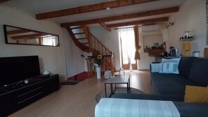 Een woonkamer met een televisie, bank en een trap die naar een keuken leidt.