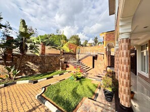 A courtyard with a paved walkway, a small lawn, and a staircase leading to a building entrance.