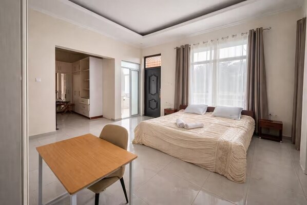 A hotel room with a bed, a desk, a chair, a wardrobe, and a door.