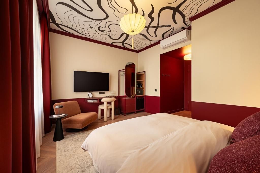 Una habitación de hotel con una cama, televisión, escritorio, silla y puerta roja.
