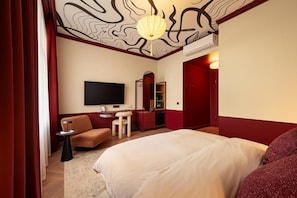 A hotel room with a bed, a TV, a desk, a chair, and a red door. - TWENTYSEVEN Boutique (Budapest)
