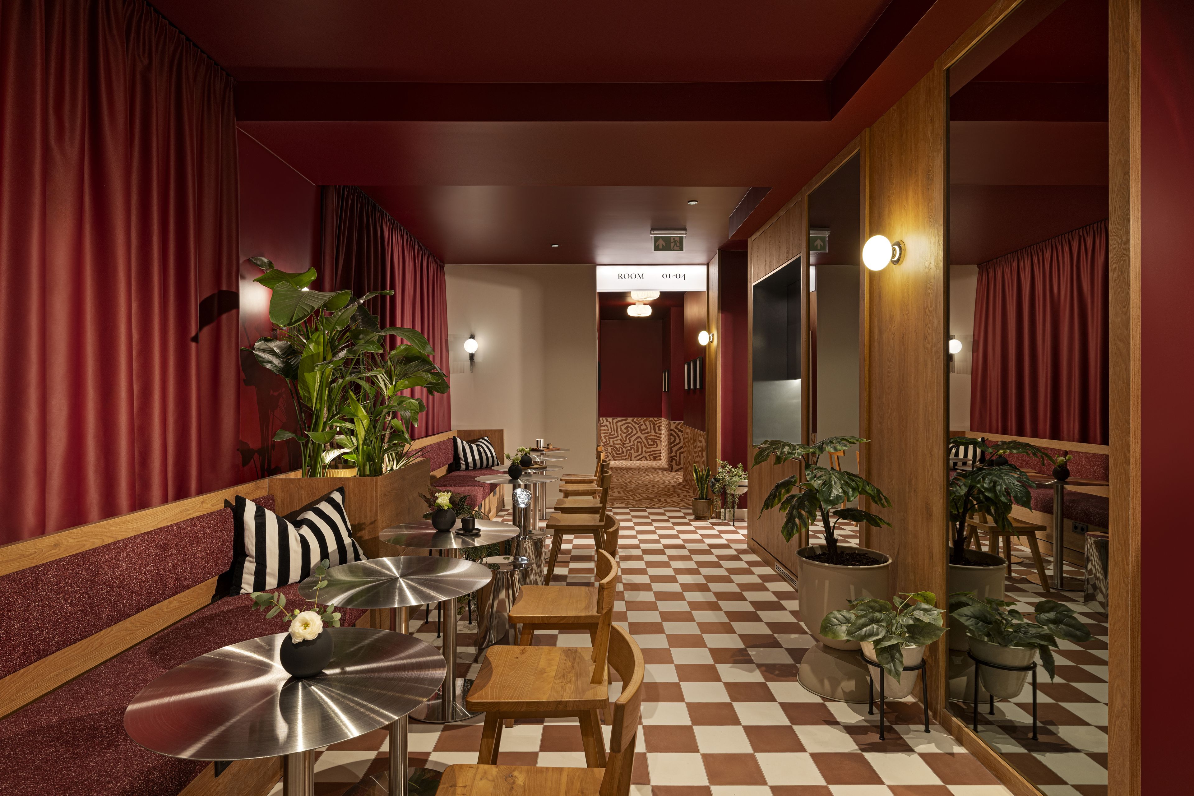 Un hall de hotel con piso de cuadros, cortinas rojas y una zona de estar con mesas y sillas.