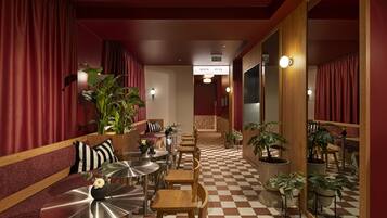 Un hall de hotel con piso de cuadros, cortinas rojas y una zona de estar con mesas y sillas.