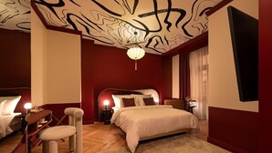 A bedroom with a large bed, a cat tree, a desk, and a ceiling with abstract designs. - TWENTYSEVEN Boutique (Budapest)