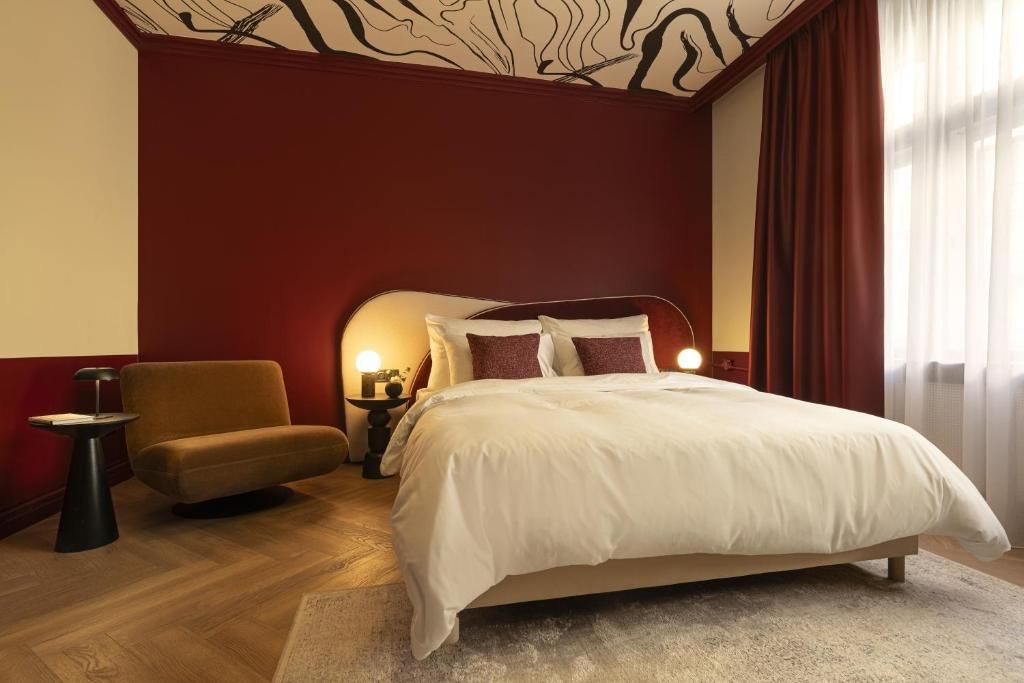 Un dormitorio con una cama grande, una mesita de noche, una silla y un tocador con una lámpara.