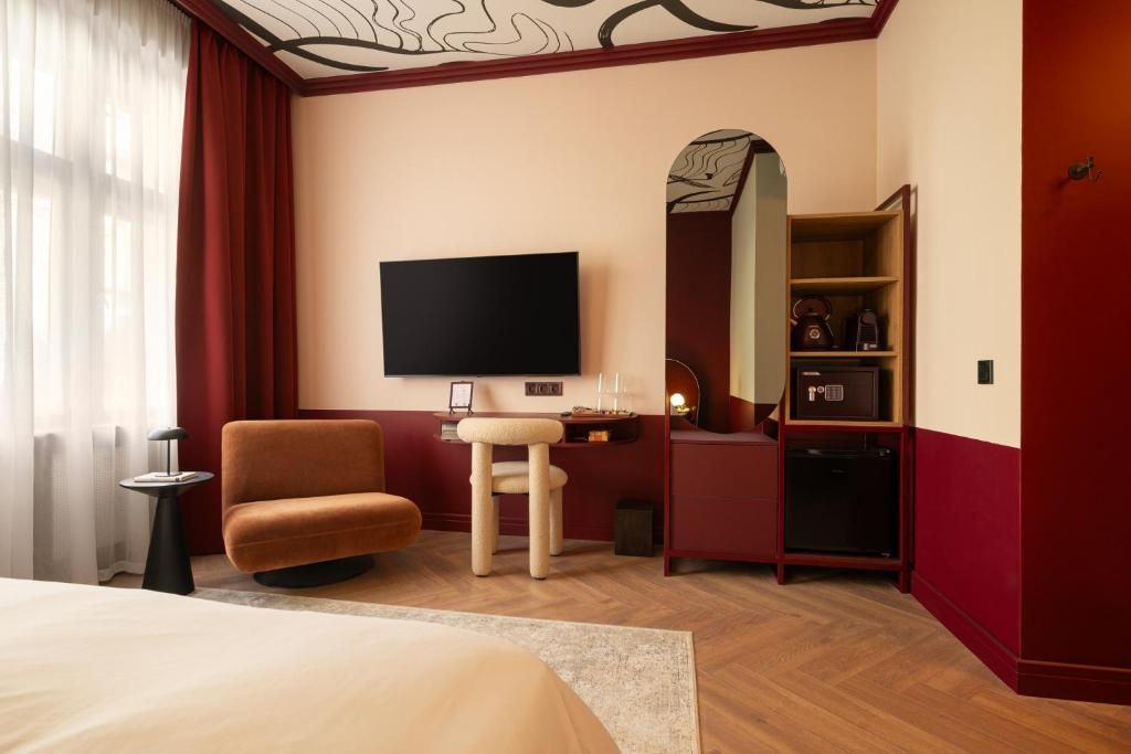 Habitación de hotel con cama, sofá, televisión, escritorio con espejo y minibar.