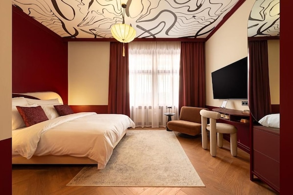 Una habitación de hotel con cama, escritorio, silla, televisor y techo estampado.