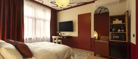 Une chambre d’hôtel dotée d’un grand lit, d’un bureau avec un téléviseur à écran plat, d’une armoire et d’un mini-bar.