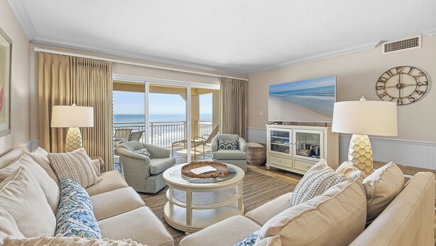 A living room with a sofa, armchairs, a coffee table, a lamp, a clock, and a painting. - 🌊Beachfront Stunner | Panoramic Ocean Views | Great Amenities | Sandpiper 514🌊 (New Smyrna Beach)