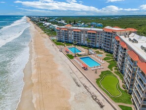 A beachfront hotel with multiple swimming pools, a beach, and lush greenery. - 🌊Beachfront Stunner | Panoramic Ocean Views | Great Amenities | Sandpiper 514🌊 (New Smyrna Beach)