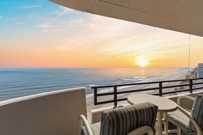 Een balkon met uitzicht op de oceaan bij zonsondergang, met een tafel en stoelen.