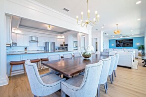 A spacious kitchen with white cabinetry, a central island, and a dining area with a large wooden table and matching chairs. - Barrett's Landing 7-bedroom Gulf Front Retreat!Large Private Beach! Sleeps 24! (Gulf Shores)