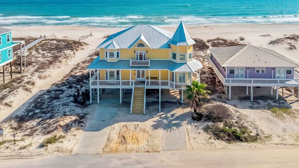 Uma casa à beira-mar com varanda, escadaria que dá para a entrada principal e vista para o oceano.
