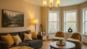 A living room with a sofa, armchairs, a coffee table, a guitar, and a painting on the wall. - Muskoka Stay in Downtown Huntsville with Firepit (Huntsville)