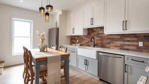 A modern kitchen with white cabinets, a brick backsplash, stainless steel appliances, and pendant lighting. - Muskoka Stay in Downtown Huntsville with Firepit (Huntsville)