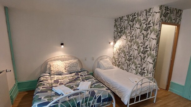 A bedroom with two metal bunk beds, a wooden floor, a radiator, and a floral wallpaper. - Les Marais Comtois (Saône)