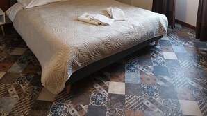 A neatly made bed with white linens and towels, a hanging light fixture, a patterned floor, and a window with curtains. - Les Marais Comtois (Saône)