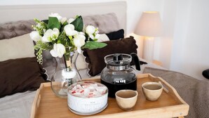 Ein Holztablett mit einer Kaffeekanne, einem Vorratsbehälter und zwei Tassen auf einem Bett mit Kissen und einem Blumenstrauß.