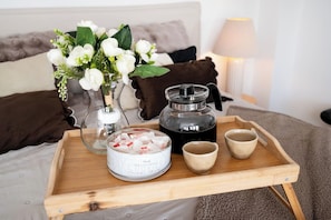 A wooden tray with a coffee pot, a canister, and two cups on a bed with pillows and a vase of flowers. - Piotrkowska Apt - AC, Top Location - by Rentujemy (Łódź)