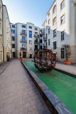 A courtyard with a central decorative wheel, surrounded by multi-story buildings with balconies and potted plants. - Piotrkowska Apt - AC, Top Location - by Rentujemy (Łódź)