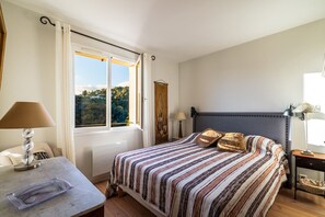 Ein Schlafzimmer mit Bett, Nachttischen, einem Fenster mit Vorhängen und Blick ins Freie.