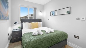 Een moderne slaapkamer met een bed, nachtkastje, lamp en een raam.