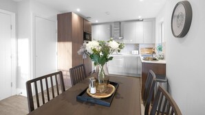 Een eethoek met een houten tafel, stoelen, een vaas met bloemen en een dienblad met zoutvaatjes.