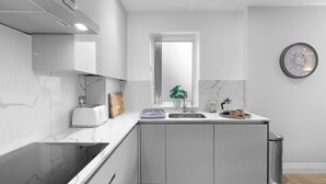 Een moderne keuken met witte kasten, een marmeren aanrecht, een ingebouwde oven, een raam en een klok aan de muur.