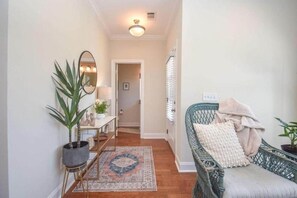 A hallway with a mirror, potted plants, a wicker chair with cushions, and a patterned rug. - Auburn Zen Den-Close to Campus (Auburn)