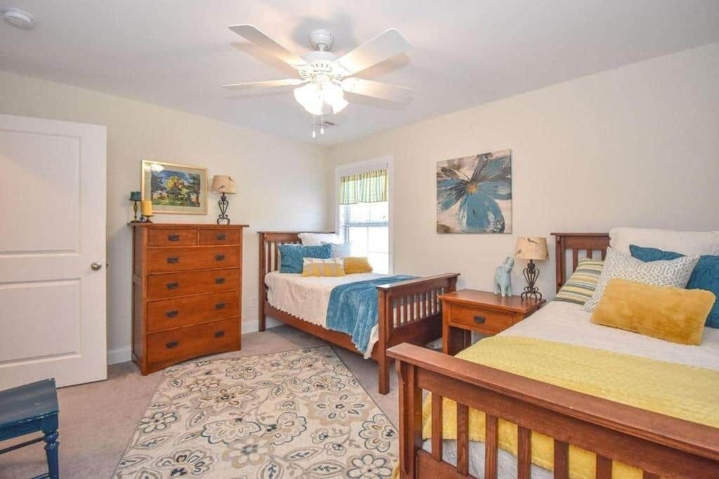 Une chambre à coucher comprenant un lit, une commode, une table de chevet, un ventilateur de plafond et une fenêtre.
