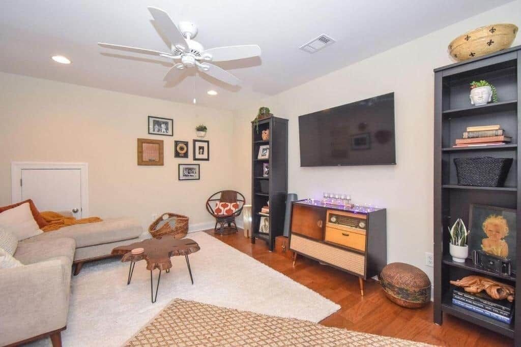 A living room with a sofa, a coffee table, a TV, a bookshelf, and a ceiling fan.