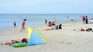 A beach with people sunbathing, a tent, and beachgoers in the water. - Feriendorf an der Ostsee, Wohlenberg (Klütz)