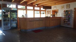 A reception area with a wooden reception desk, a vending machine, and a wall-mounted information board. - Feriendorf an der Ostsee, Wohlenberg (Klütz)