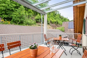 Ein Balkon mit Holzmöbeln, einem Blumentopf und einer Glaskonstruktion.