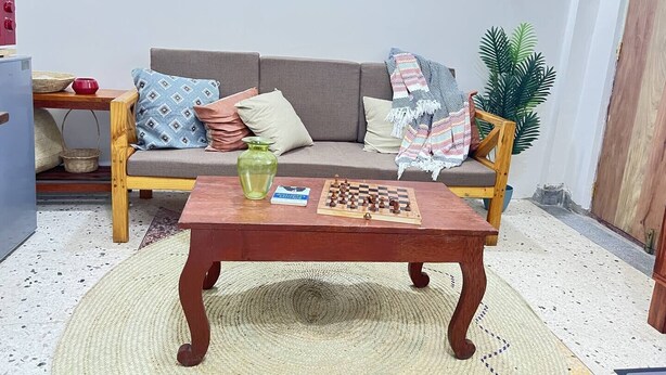 Un salon avec un canapé, une table basse en bois, un jeu d’échecs et un tapis tissé.