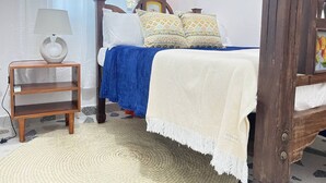 Une chambre à coucher avec un lit à baldaquin, une table de chevet avec une lampe, un tapis tissé et un mur orné d’un tableau.