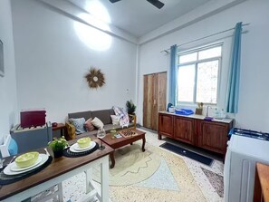 A living room with a sofa, coffee table, and a dining area with a table and chairs. There is a window with curtains, a ceiling fan, and a door. - Cozy 1-bedroom apartment in wonderful Paje with AC (Paje)