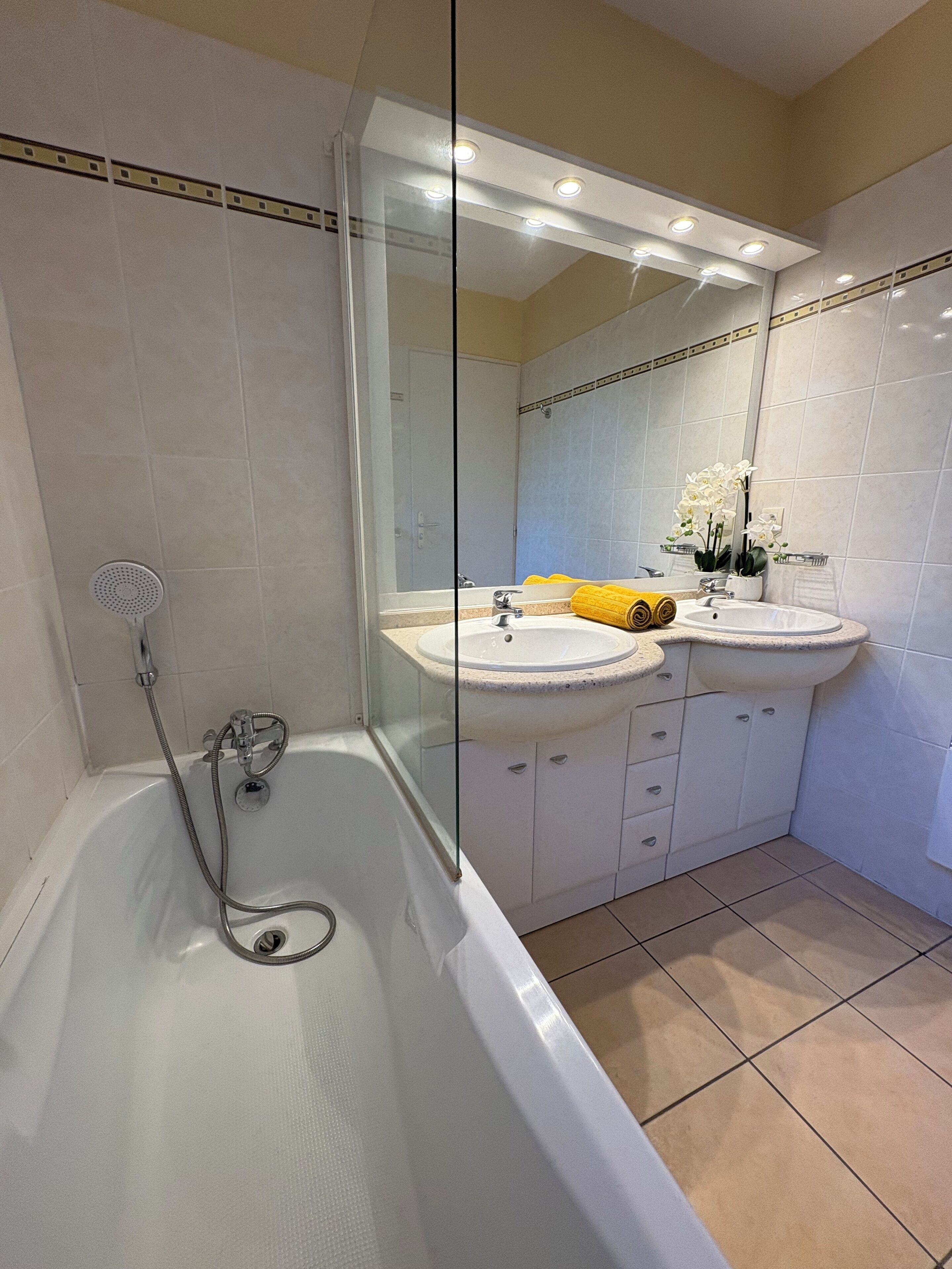 Un baño con ducha de vidrio, dos lavamanos y una bañera.