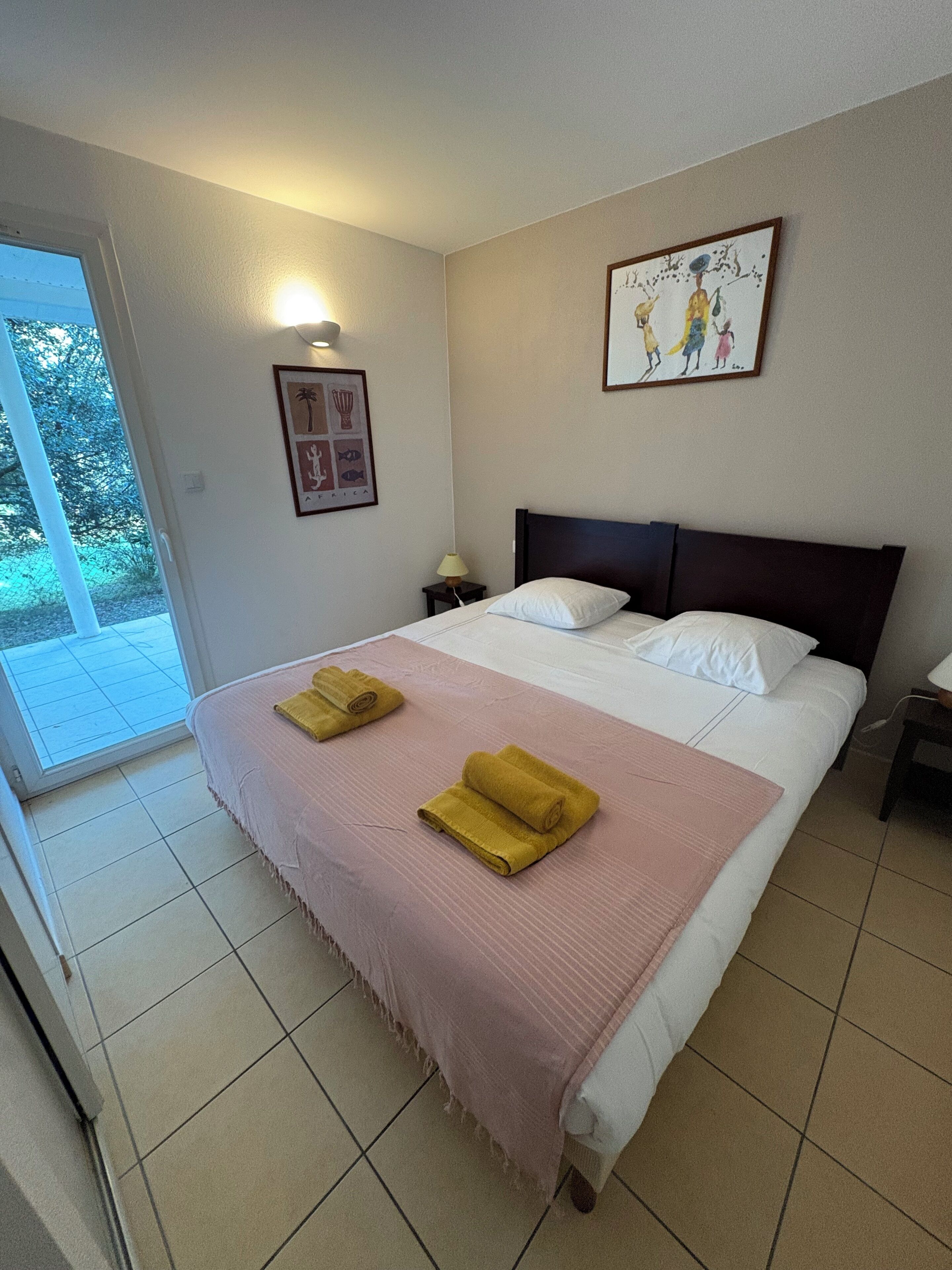 Een hotelkamer met een bed, nachtkastje, lamp, raam en deur.