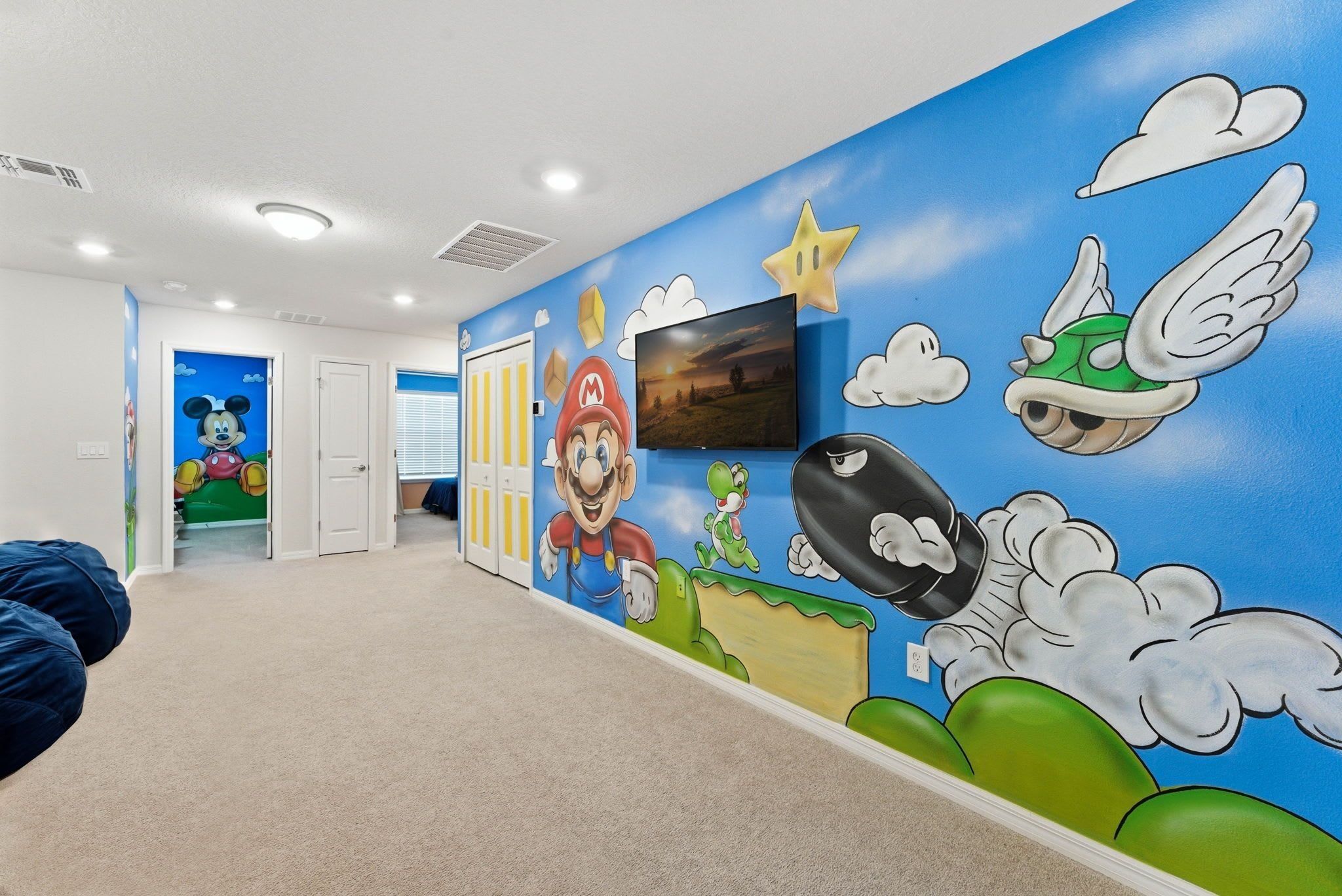 Ein Zimmer mit einer Wandmalerei zum Thema Mario, einem Fernseher und einer Tür zu einem anderen Raum.