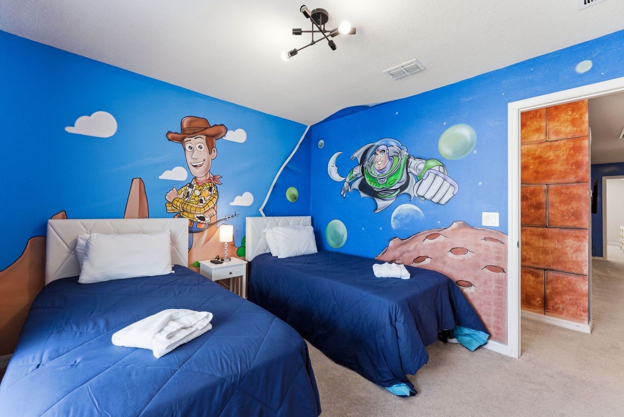 A room with two beds, a mural of Woody and Buzz Lightyear, and a view of the outside.