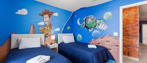 A room with two beds, a mural of Woody and Buzz Lightyear, and a view of the outside.