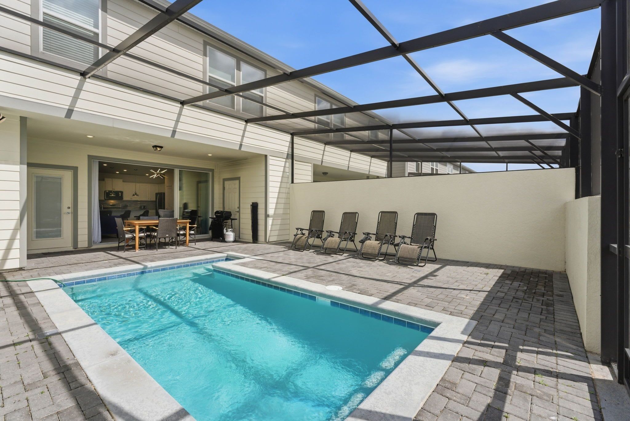 A swimming pool with a covered patio area, a dining table, and chairs.