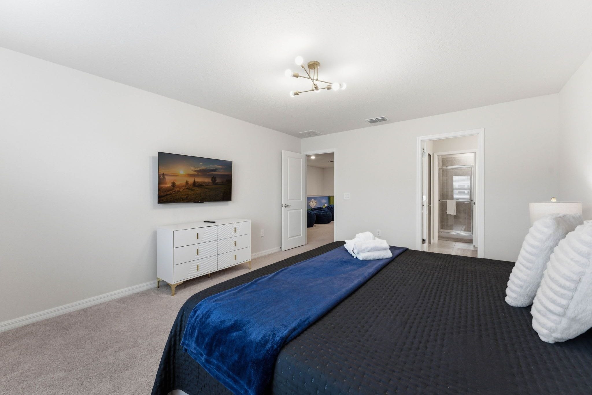 A bedroom with a bed, a dresser, a painting, and a door leading to a bathroom.