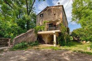 A rustic two-story house with a balcony, surrounded by greenery and a stone wall. - Holiday Home “Le Moulin de Mirande” with Terrace, Private Garden & Wi-Fi (La Tour-sur-Orb)